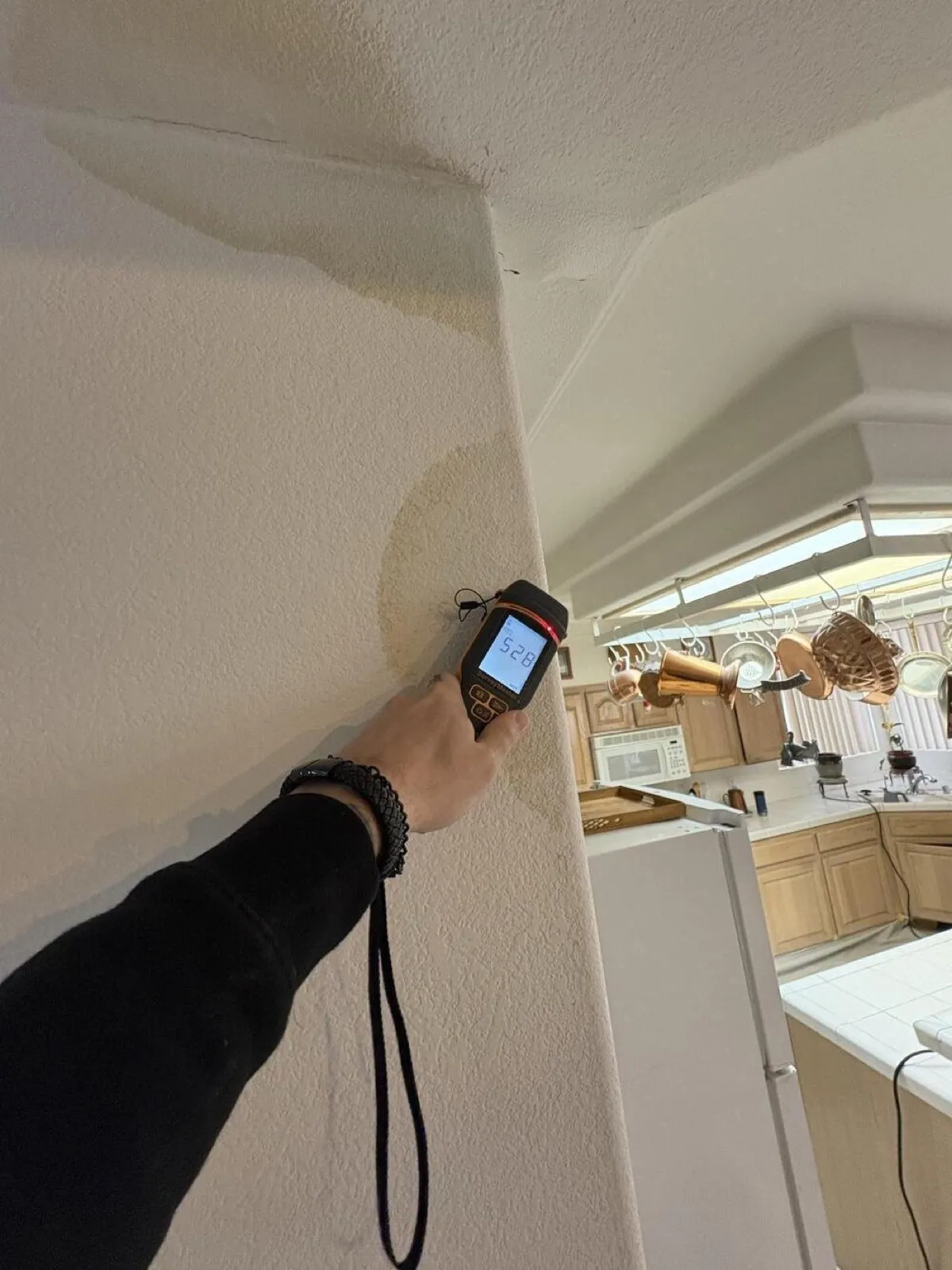 Moisture meter on a water-stained kitchen wall, water damage repair in Las Vegas