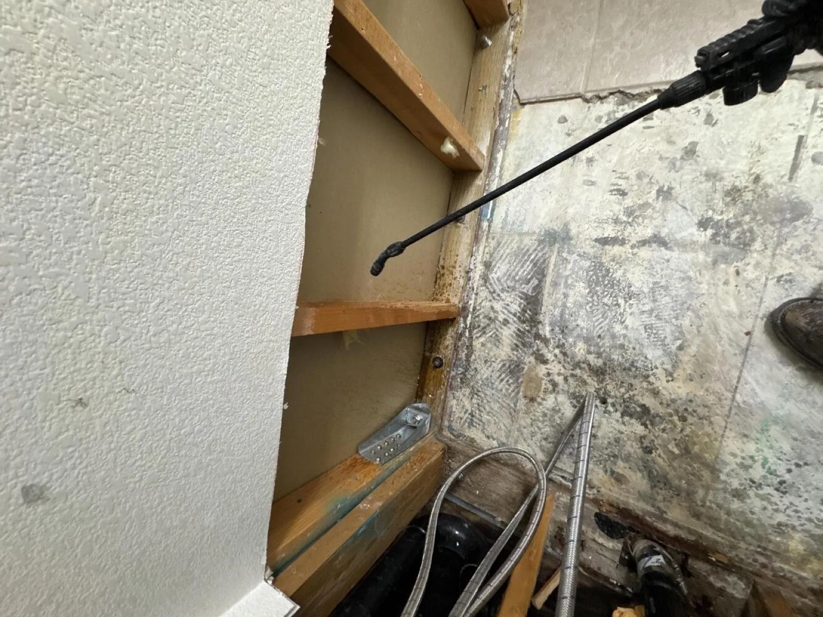 Spray wand applying treatment inside a moldy wall cavity, mold remediation in Las Vegas