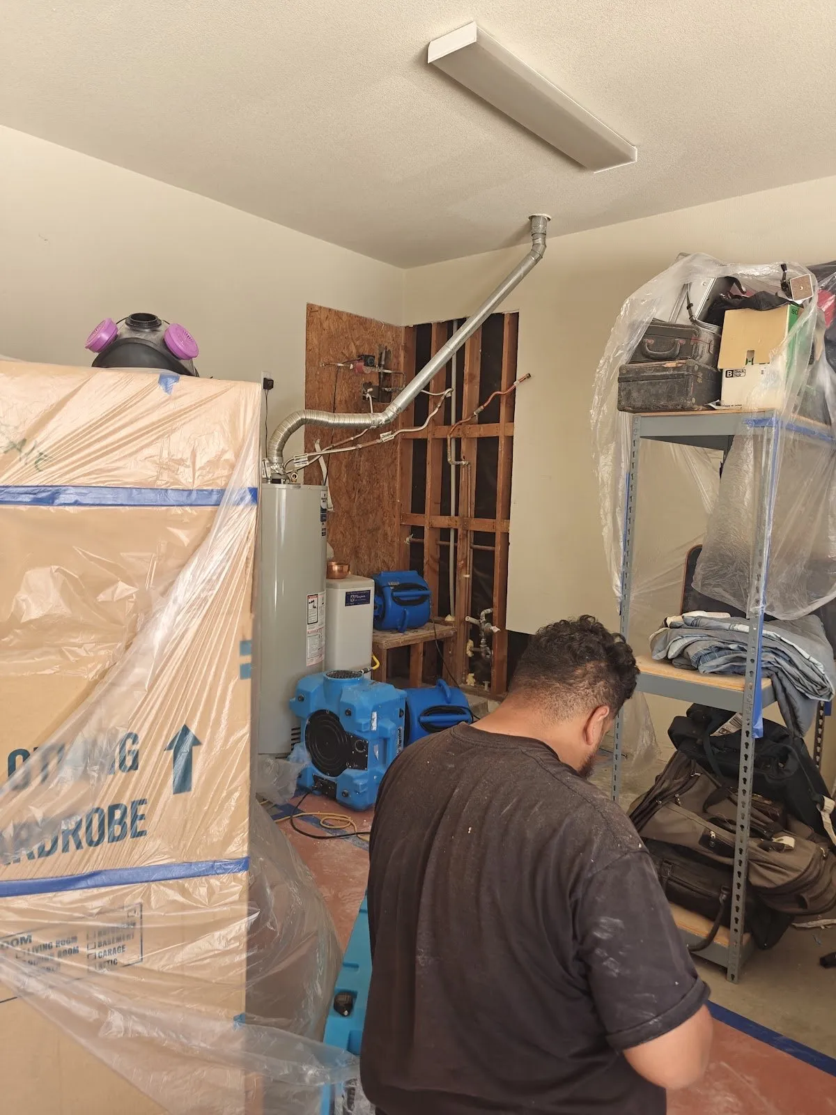 Technician working in a garage with belongings wrapped in plastic and air movers running, water damage restoration in Las Vegas