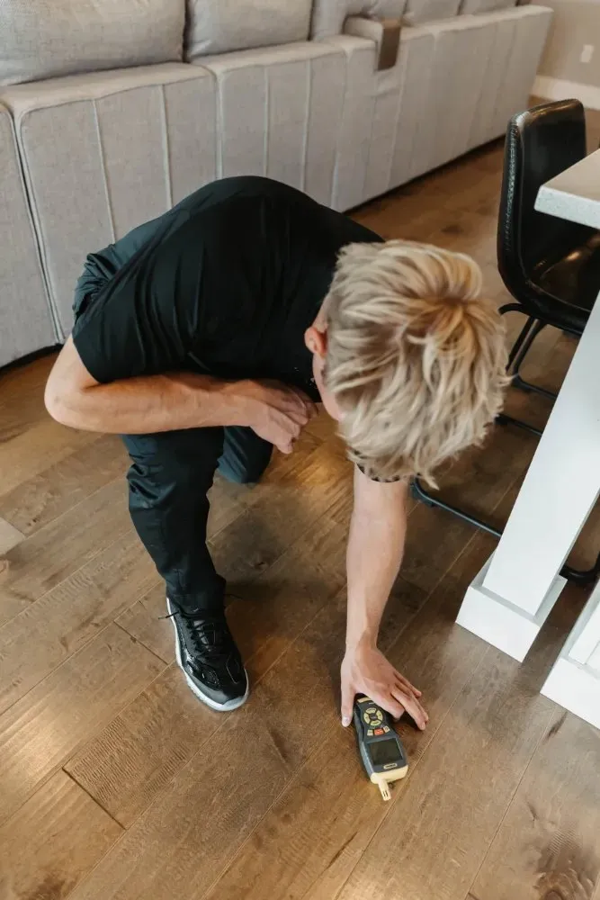 Technician crouching to take a moisture reading on a wood floor, water damage restoration in Summerlin, NV