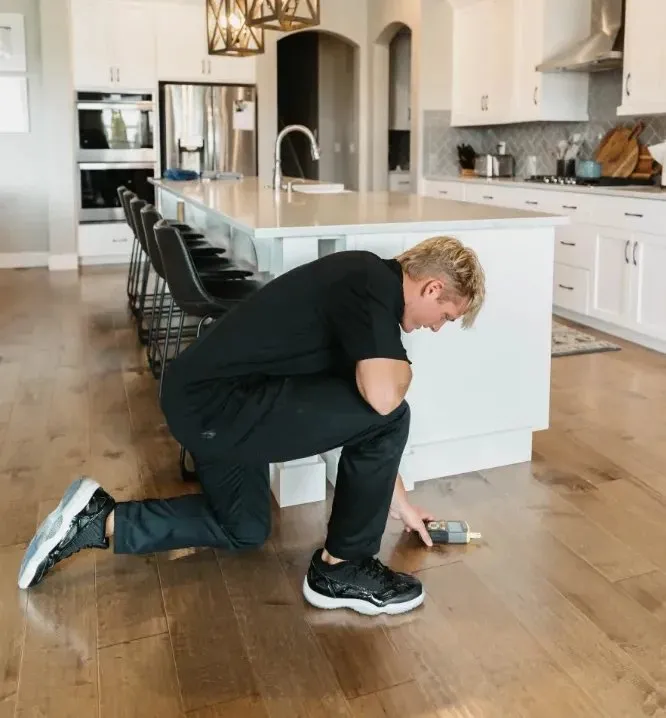 Technician kneeling on a wood kitchen floor to take a moisture reading, water damage restoration company in Las Vegas